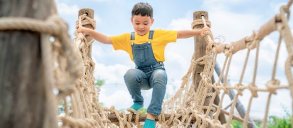 a young child walks across a rope bridge at a playground